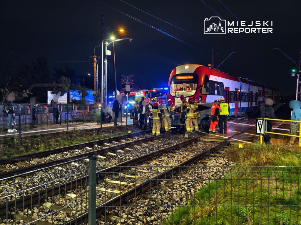 Strażacy i służby ratunkowe pracują przy czerwono-białym tramwaju na torowisku nocą.
