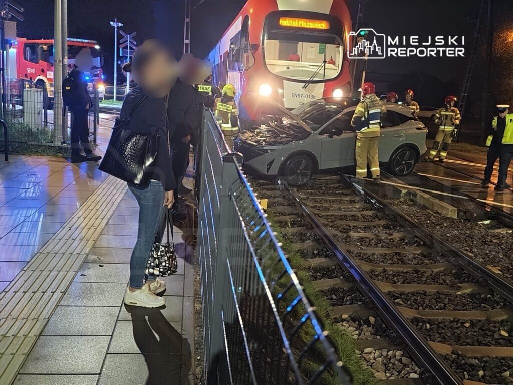 Uszkodzony samochód stoi na torach przed tramwajem, a strażacy zabezpieczają miejsce nocnego wypadku.
