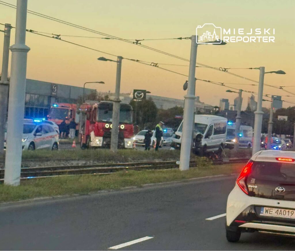 Służby ratunkowe i czerwony tramwaj stoją przy torowisku, obok białego busa i radiowozów z włączonymi światłami.