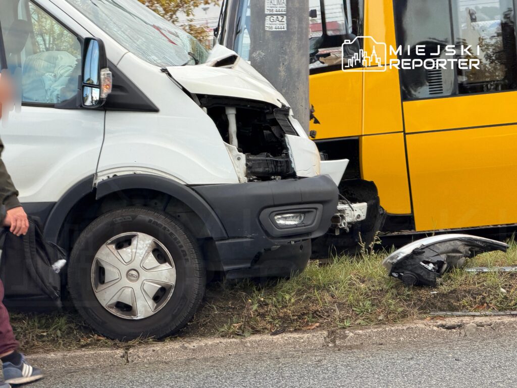 Uszkodzony biały bus stoi przed żółtym tramwajem po zderzeniu, z rozbitym przodem i oderwanymi częściami na poboczu.