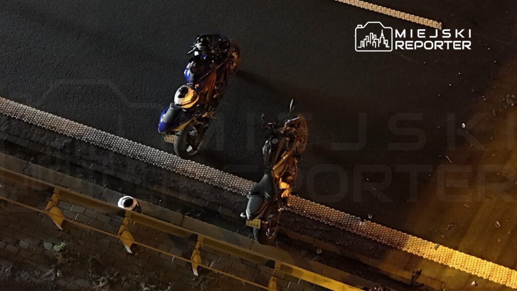 Dwa motocykle stoją przy krawężniku na nocnej ulicy widzianej z góry.