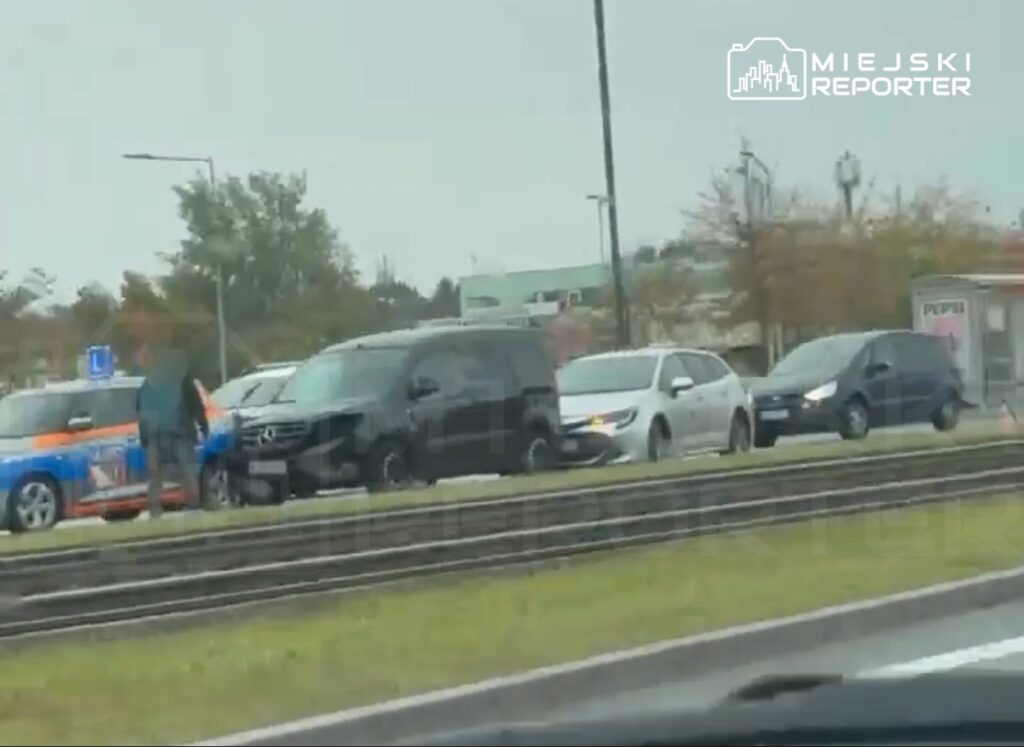 Kilka samochodów stoi na pasie drogowym obok torowiska tramwajowego, a przy jednym z nich stoi osoba.