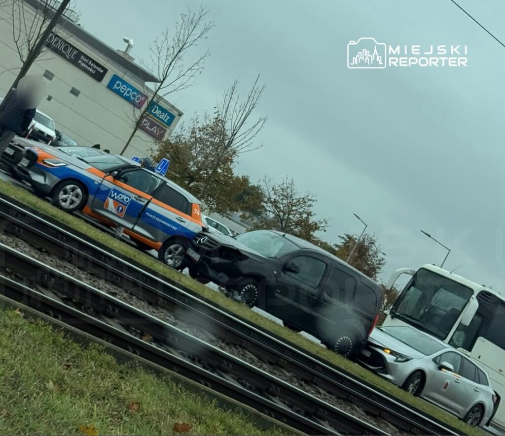Samochody stoją na ulicy przy torowisku tramwajowym, obok centrum handlowego z szyldem Pepco.