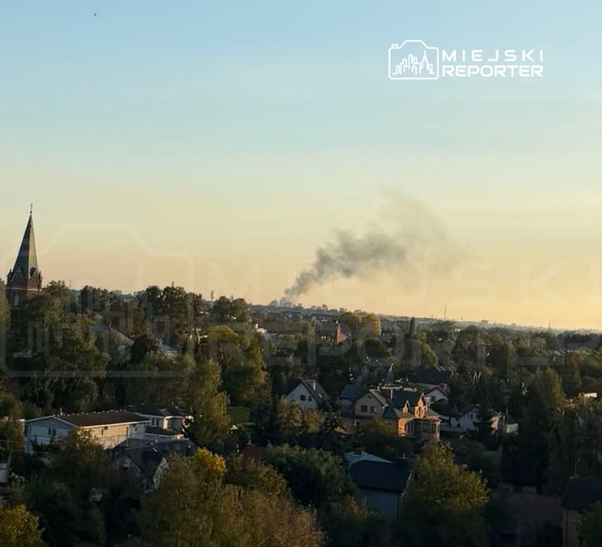 Dym unoszący się nad zabudową mieszkalną i drzewami, widoczny na tle wieczornego nieba.