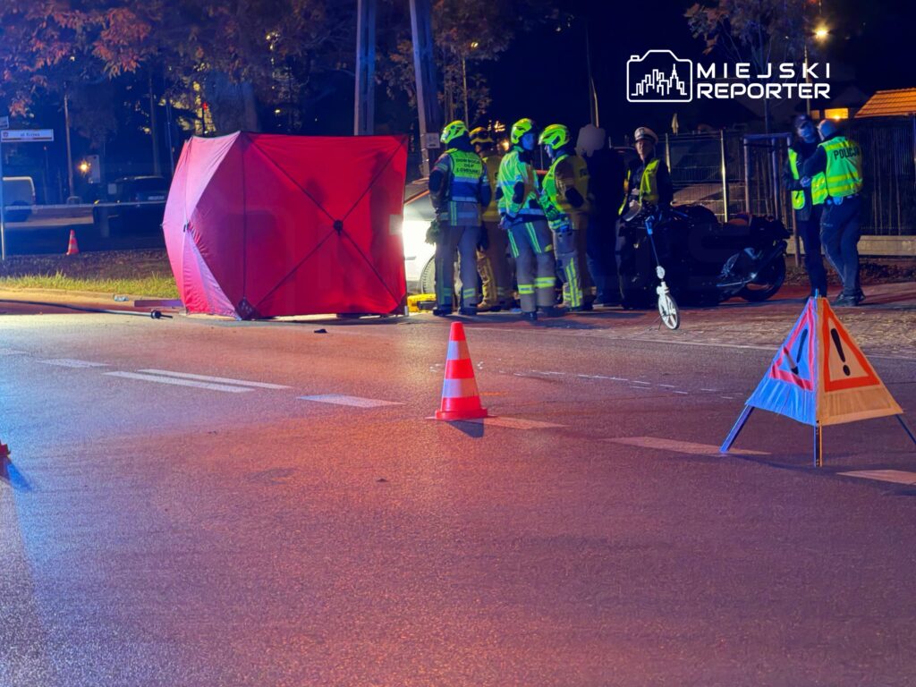 Ratownicy w odblaskowych strojach zabezpieczają miejsce zdarzenia na nocnej ulicy, osłonięte czerwonym parawanem i
