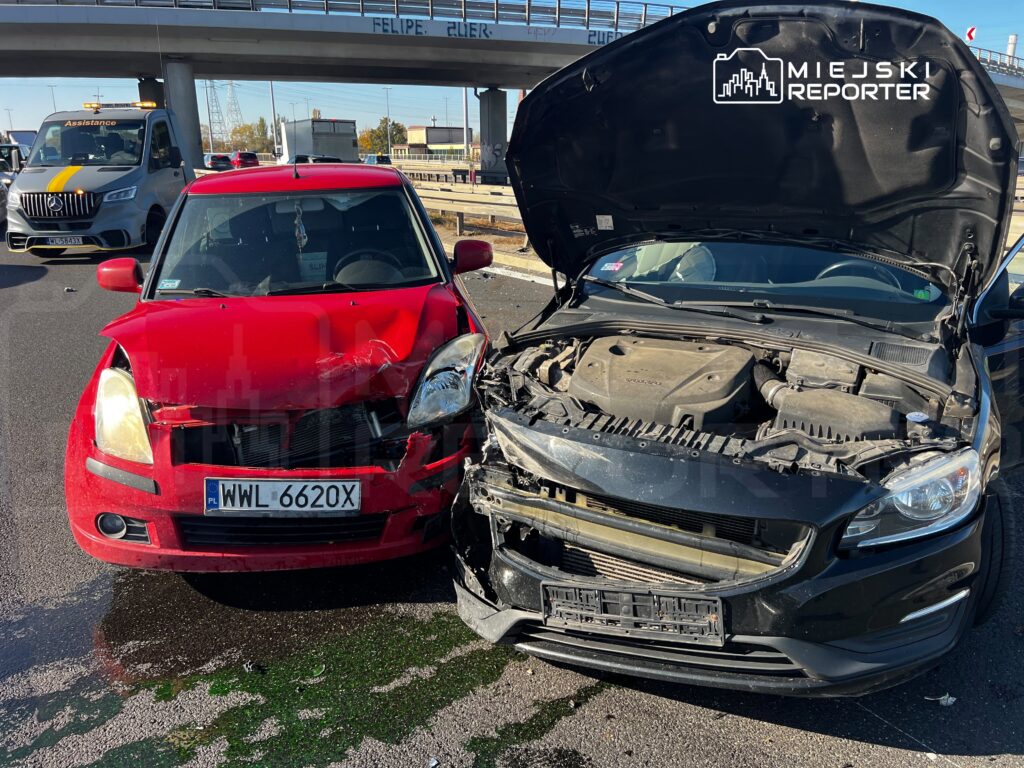 Czerwony i czarny samochód po zderzeniu, z uszkodzonymi przodami; w czarnym aucie otwarta maska, obok stoi laweta.