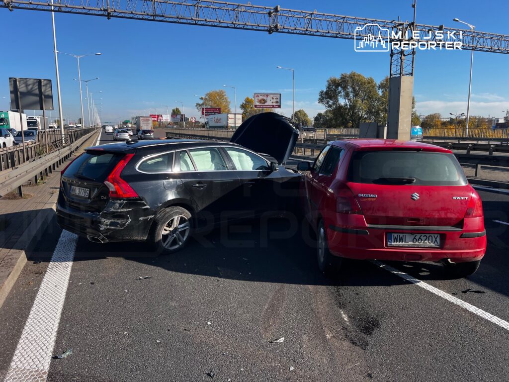 Czarny kombi i czerwony hatchback po kolizji stoją na jezdni wiaduktu, z otwartą maską czarnego auta.