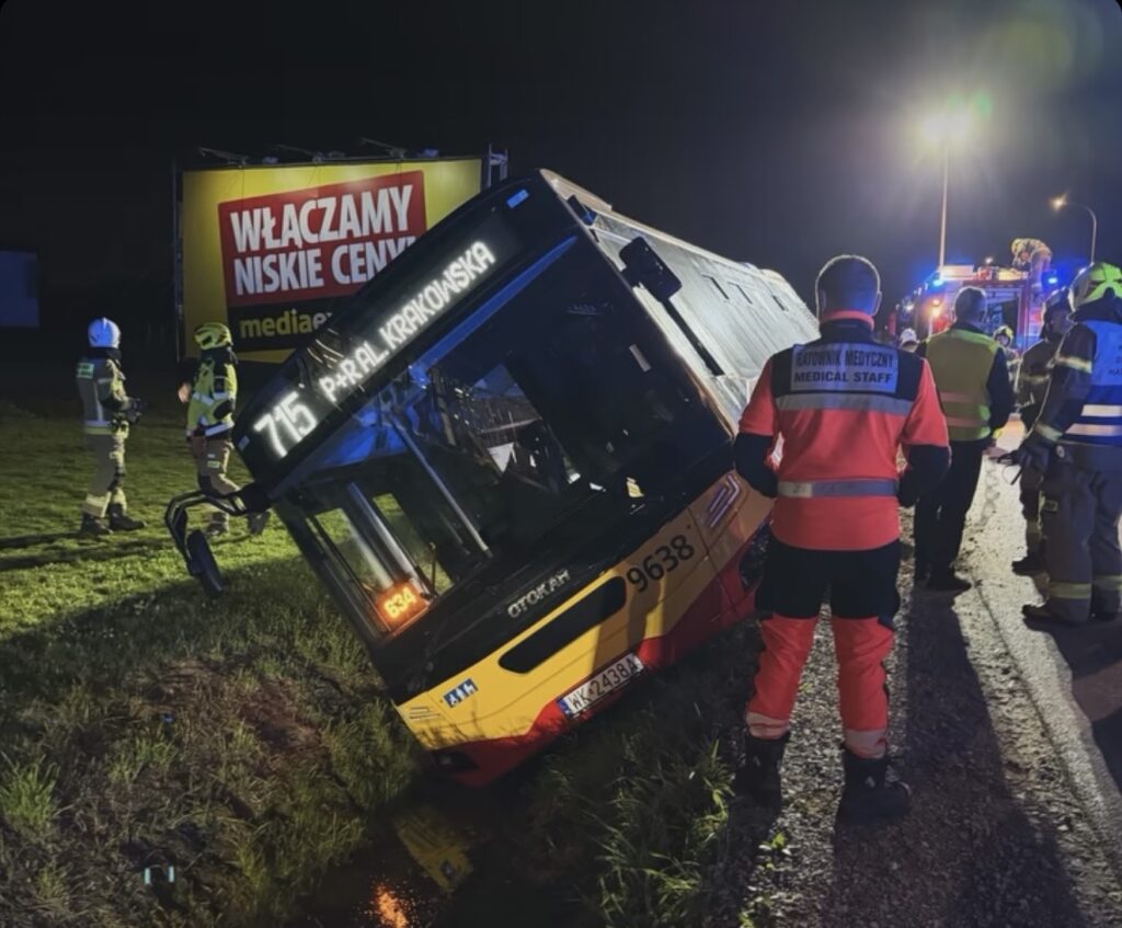 Przewrócony żółty autobus linii 715 w rowie przy drodze, obok służby ratunkowe i medyczne nocą.
