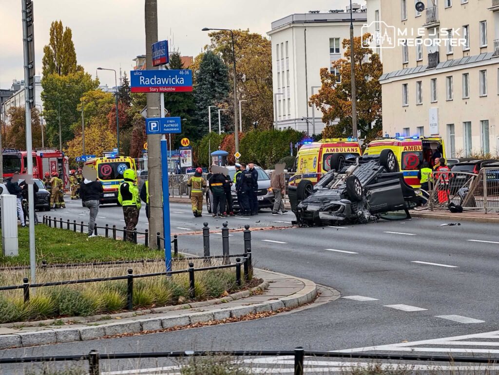 Ratownicy i policjanci zabezpieczają miejsce wypadku z przewróconym samochodem na ulicy Radawickiej.