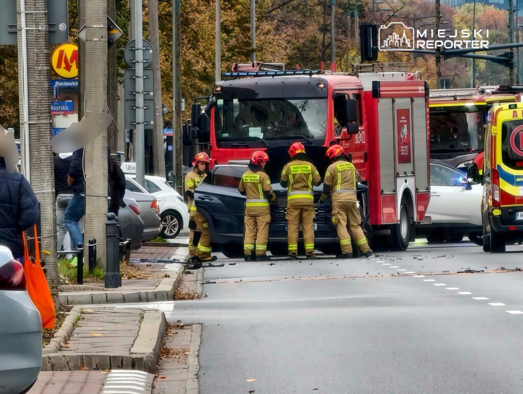 Strażacy w ubraniach ochronnych stoją przy wozie strażackim na ulicy obok karetki pogotowia.