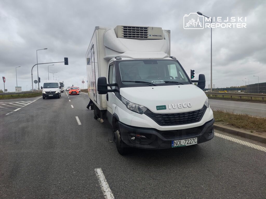Biała chłodnia Iveco stoi na pasie ruchu przy skrzyżowaniu, za nią jadą samochody.