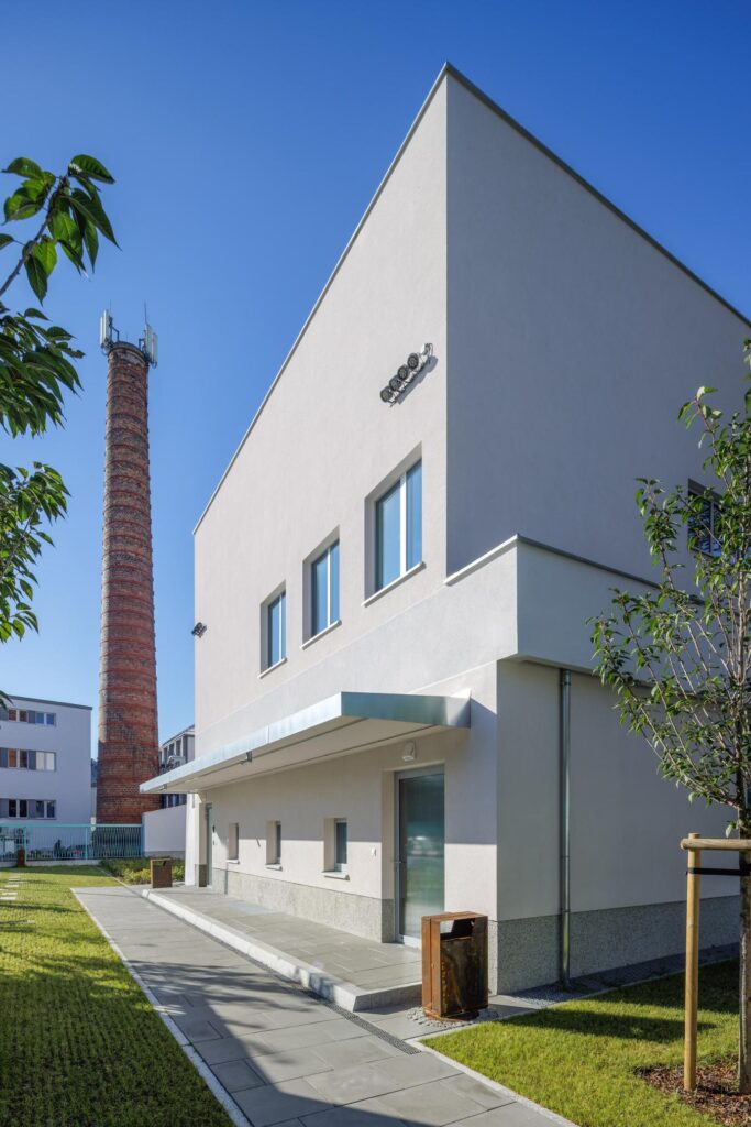 Biały, modernistyczny budynek z napisem „Kino Tęcza” i wysokim ceglanym kominem obok, w słoneczny dzień.