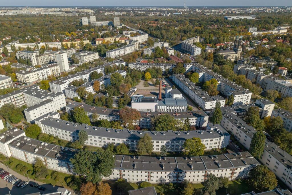 Widok z lotu ptaka na osiedle niskich bloków otoczonych drzewami i zielenią miejską.
