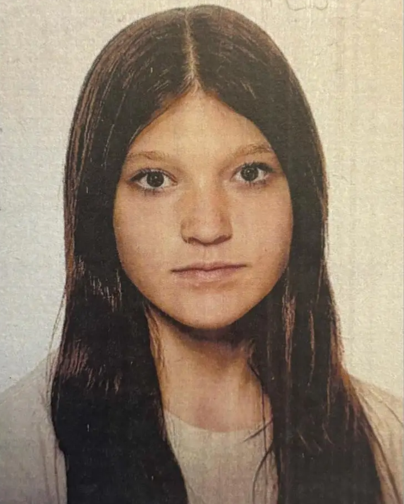 Portret dziewczynki z długimi, ciemnymi włosami, patrzącej prosto w obiektyw na jasnym tle.