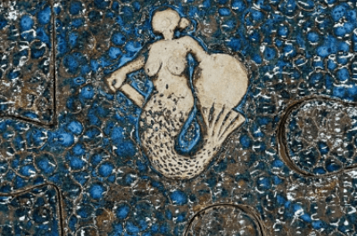 Ceramiczna mozaika z postacią syreny na tle niebieskich, nieregularnych płytek.