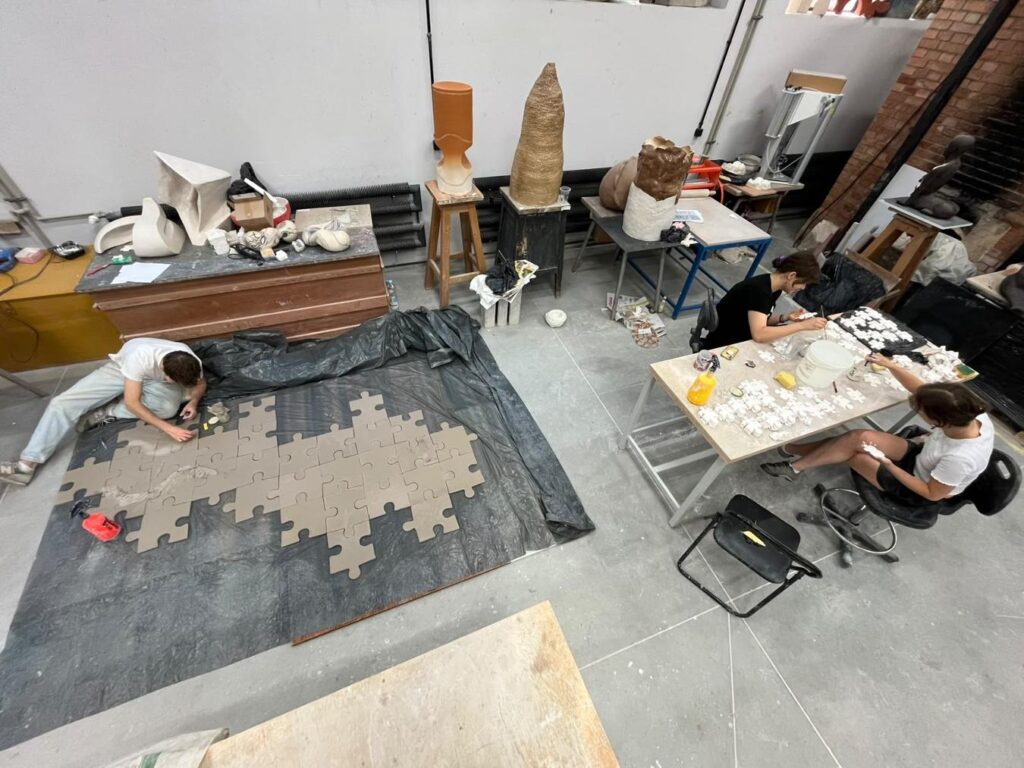 Artyści układają ceramiczne elementy mozaiki w kształcie puzzli w pracowni rzeźbiarskiej.