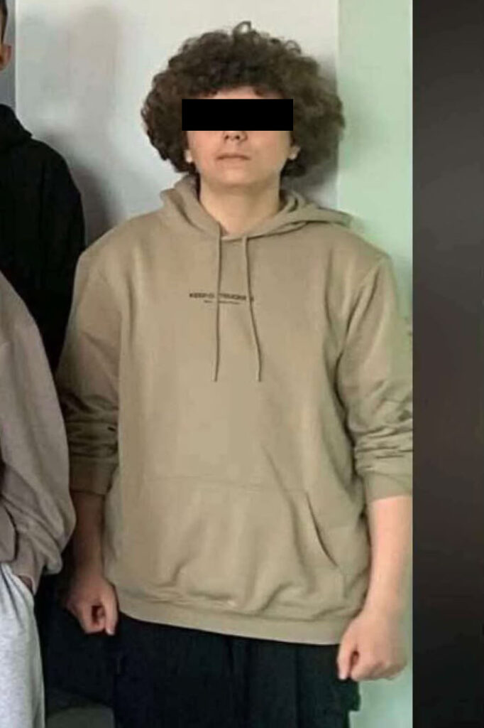 Młody mężczyzna z zasłoniętymi oczami stoi w beżowej bluzie z kapturem na tle jasnej ściany.