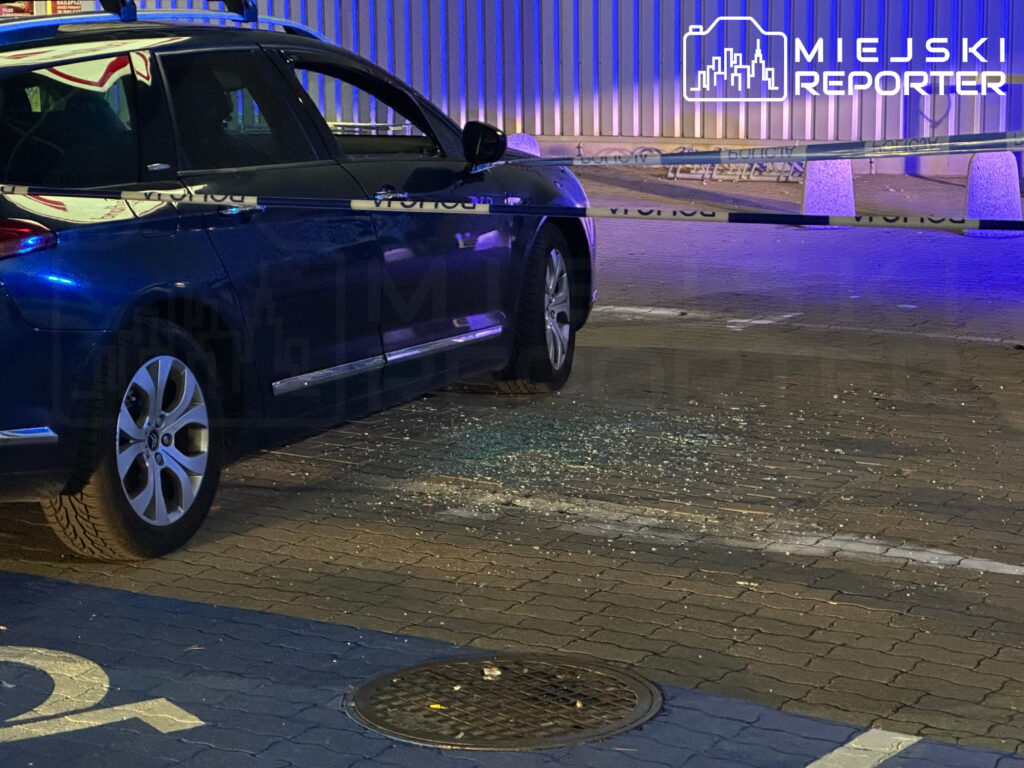 Ciemny samochód osobowy za policyjną taśmą na oświetlonym niebieskim światłem chodniku nocą.
