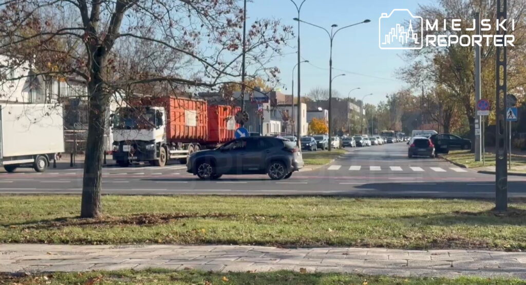 Samochody i ciężarówki stoją w korku na miejskiej ulicy przy przejściu dla pieszych.