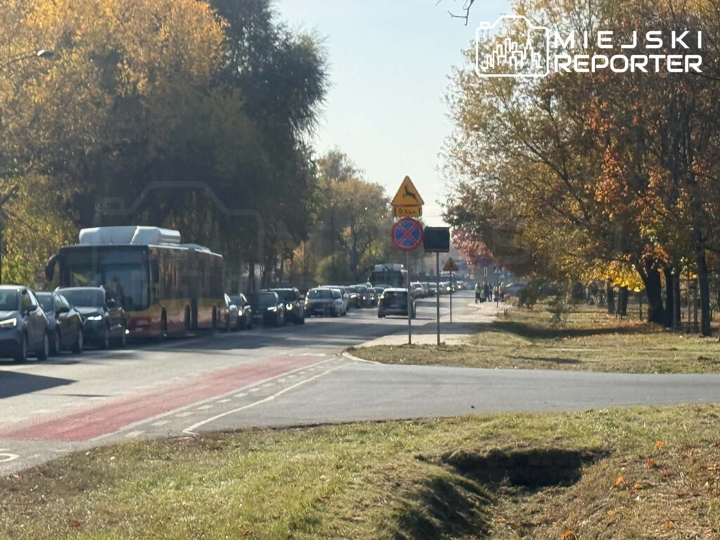 Samochody i autobus stoją w korku na ulicy wśród jesiennych drzew.