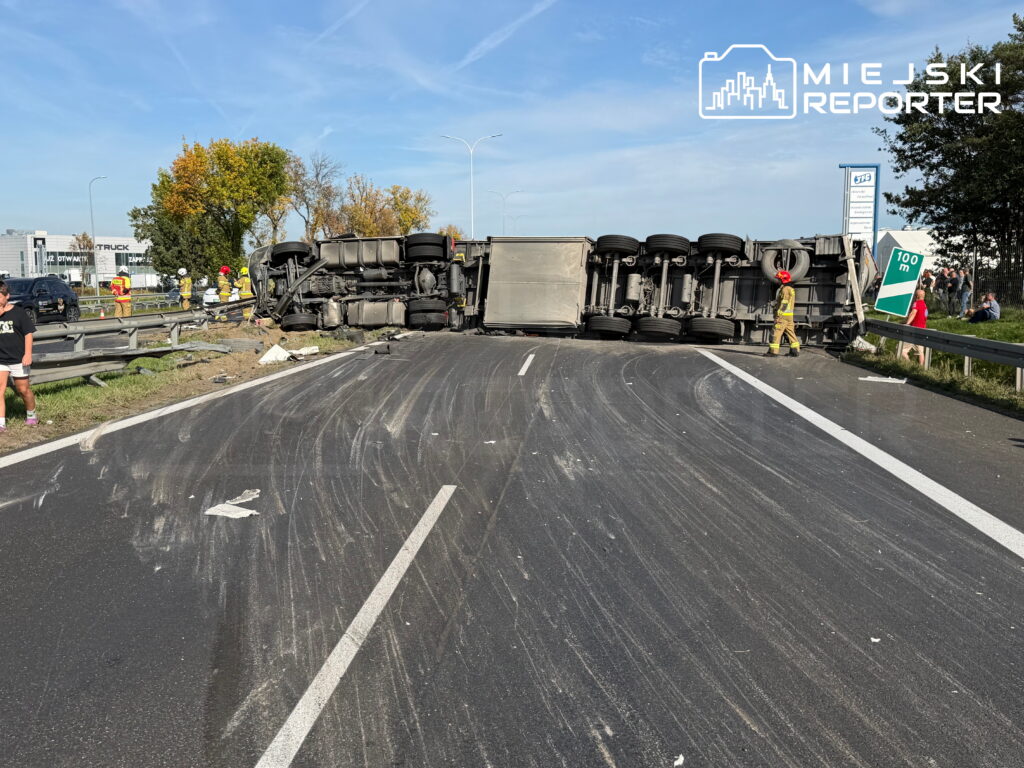 Przewrócona ciężarówka blokuje drogę, a służby zabezpieczają miejsce zdarzenia.