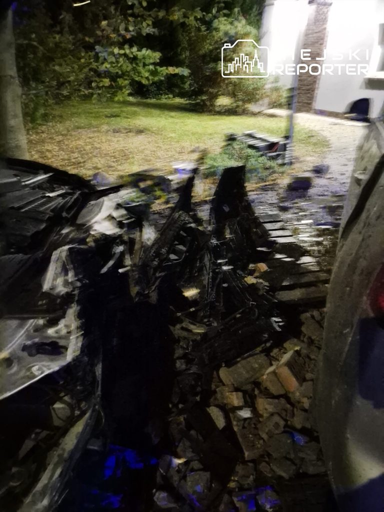 Rozbite elementy pojazdu i gruz leżą na nocnym podwórzu przy budynku po wypadku.
