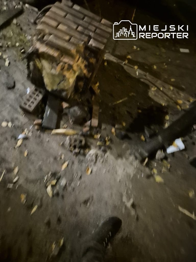 Uszkodzona drewniana ławka i porozrzucane elementy leżą na chodniku nocą.