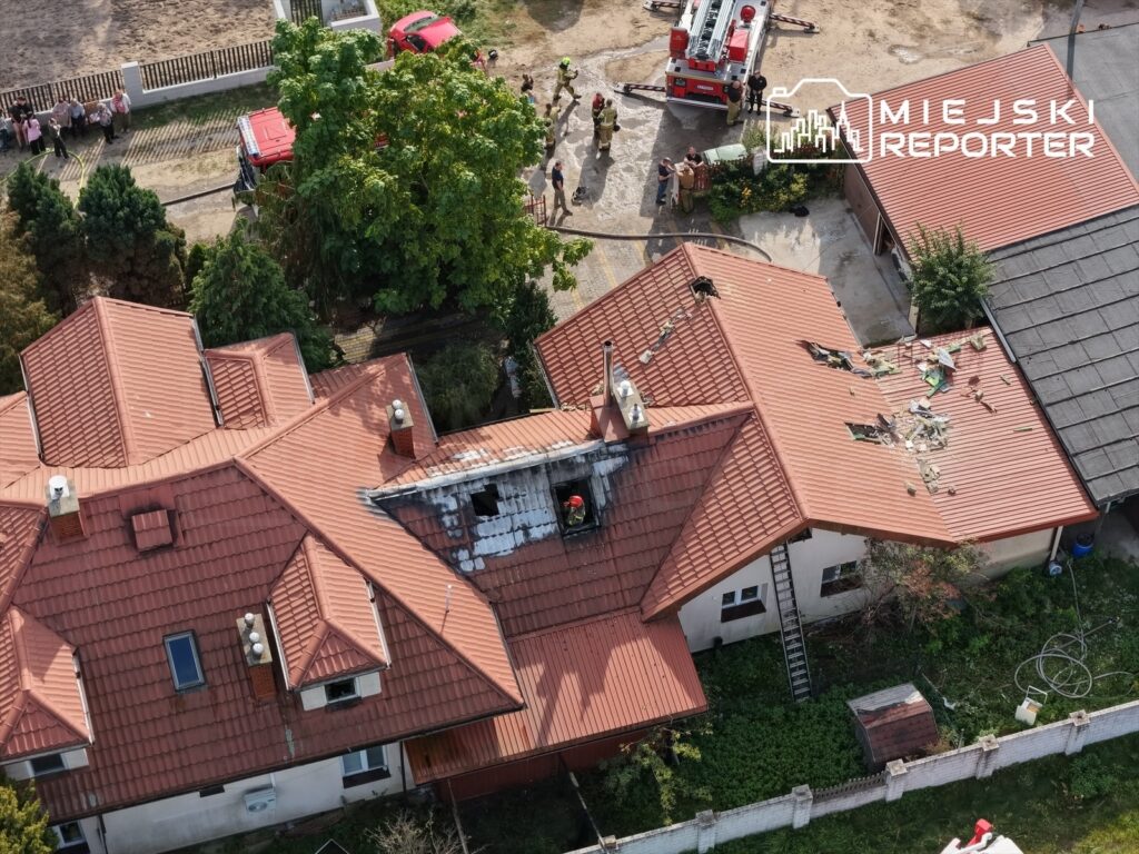 Uszkodzony przez pożar dach domu, przy którym stoją wozy strażackie i ratownicy