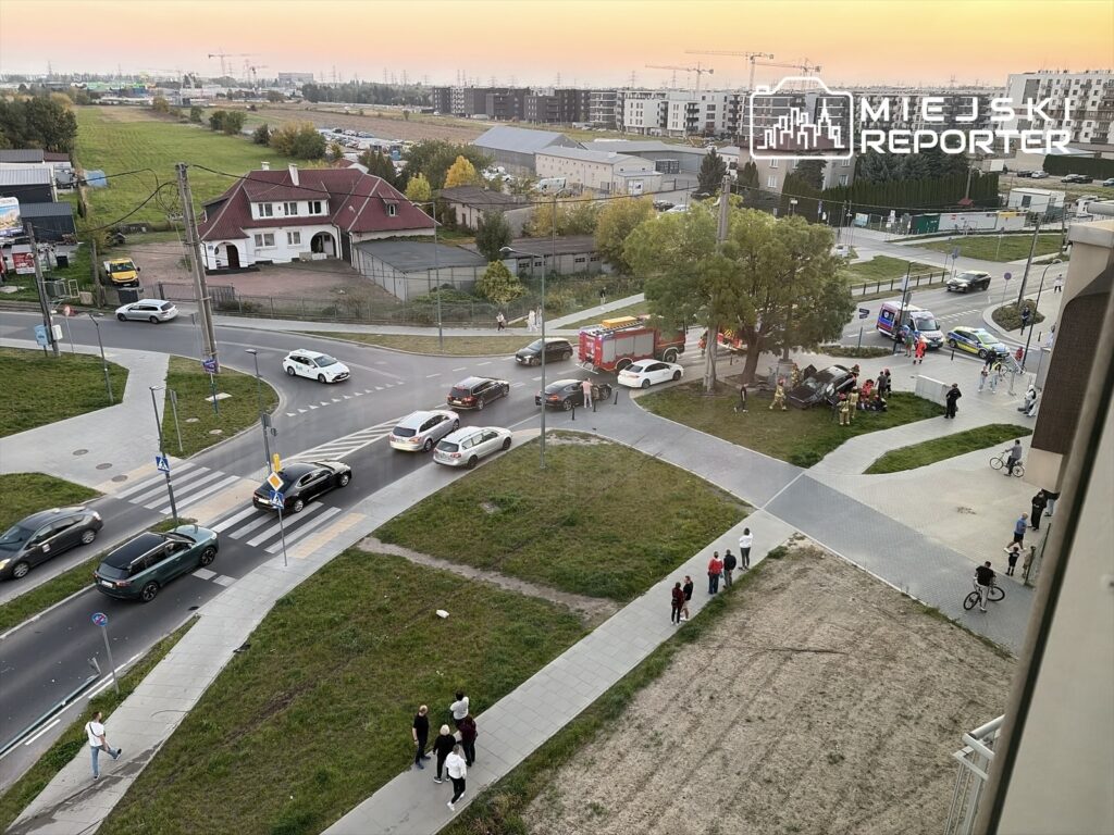 Samochody służb ratunkowych i osobowe na skrzyżowaniu obok przejścia dla pieszych, wśród zabudowy mieszkalnej.