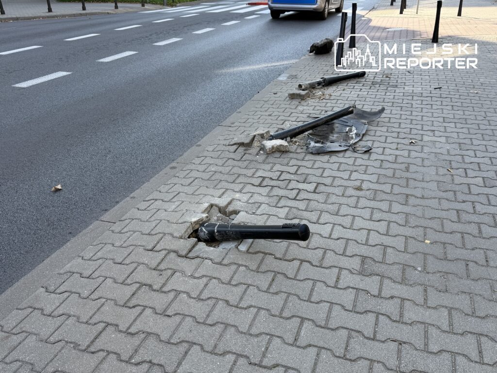 Połamane elementy słupków i barierki leżą na chodniku przy jezdni.