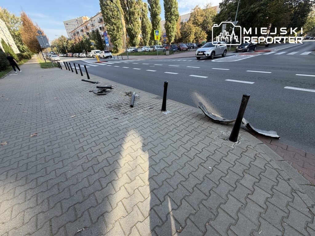 Uszkodzone i powyginane słupki leżą na chodniku przy przejściu dla pieszych obok ruchliwej ulicy.