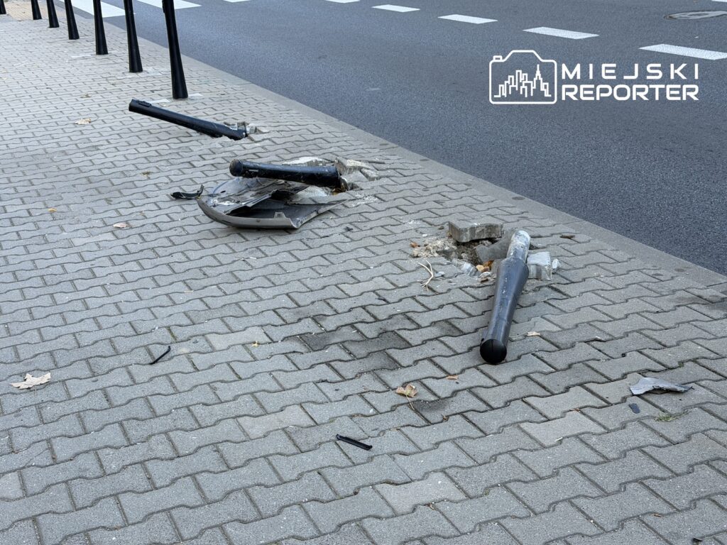 Połamane słupki i fragmenty uszkodzonej infrastruktury leżą na chodniku przy krawędzi jezdni.