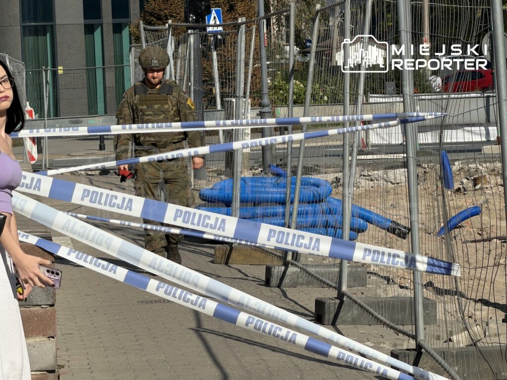 Umundurowany mężczyzna stoi za taśmami z napisem „POLICJA” przy ogrodzonym wykopie na ulicy.