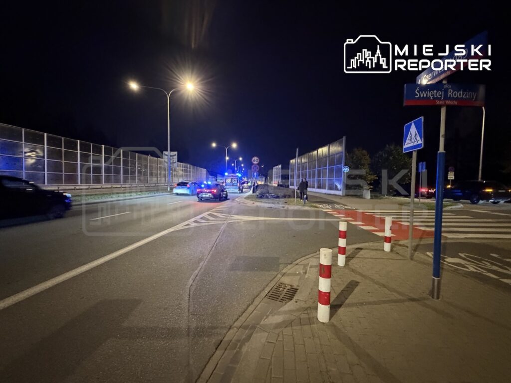 Radiowozy z włączonymi niebieskimi światłami stoją nocą na skrzyżowaniu przy przejściu dla pieszych.