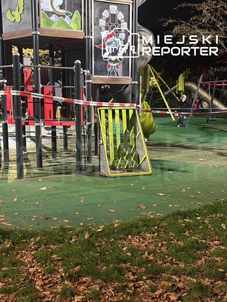 Plac zabaw z kolorową konstrukcją i zjeżdżalniami odgrodzony taśmą, nocą oświetlony przez służby.