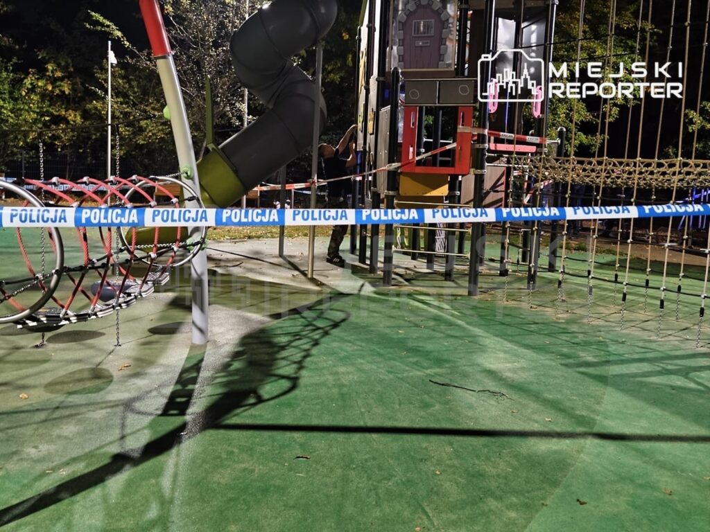 Plac zabaw z konstrukcją wspinaczkową odgrodzony niebiesko-białą taśmą policyjną z napisem „POLICJA