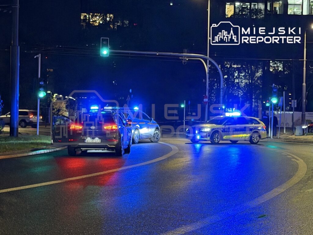 Radiowozy policji z włączonymi niebieskimi światłami blokują nocą ruch na skrzyżowaniu.