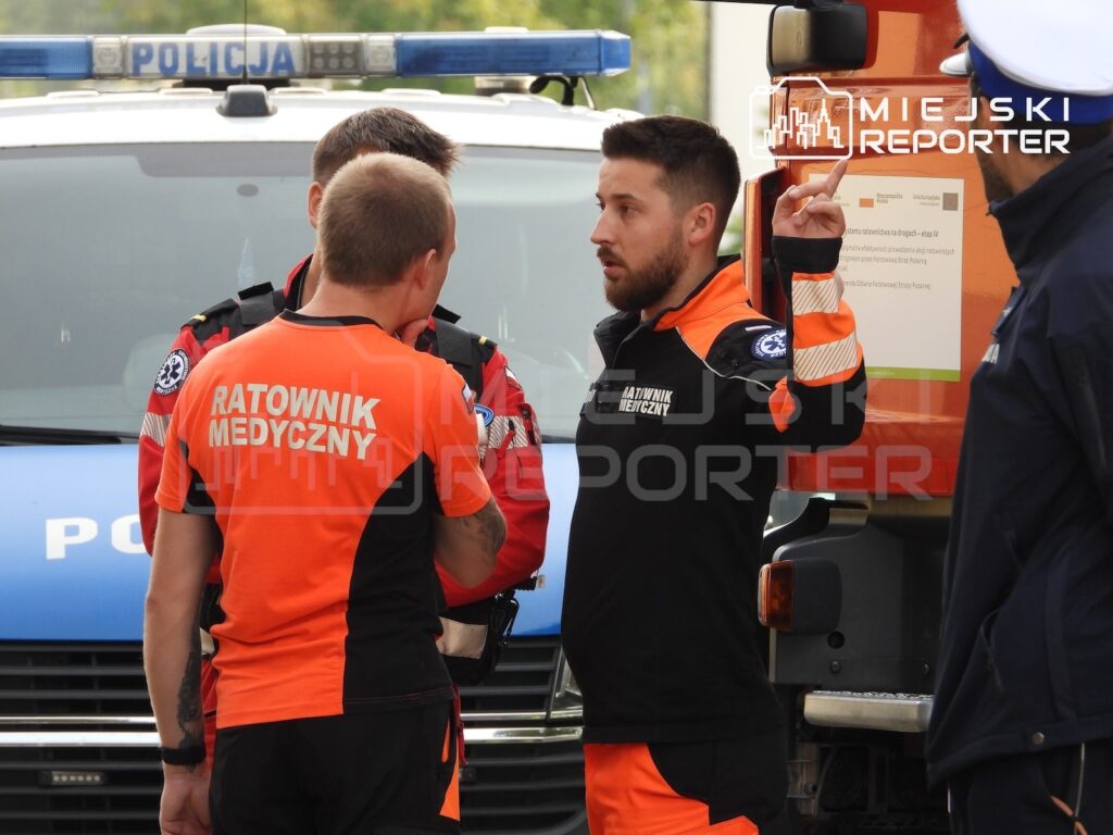 Ratownicy medyczni rozmawiają przy radiowozie i karetce pogotowia na miejscu zdarzenia