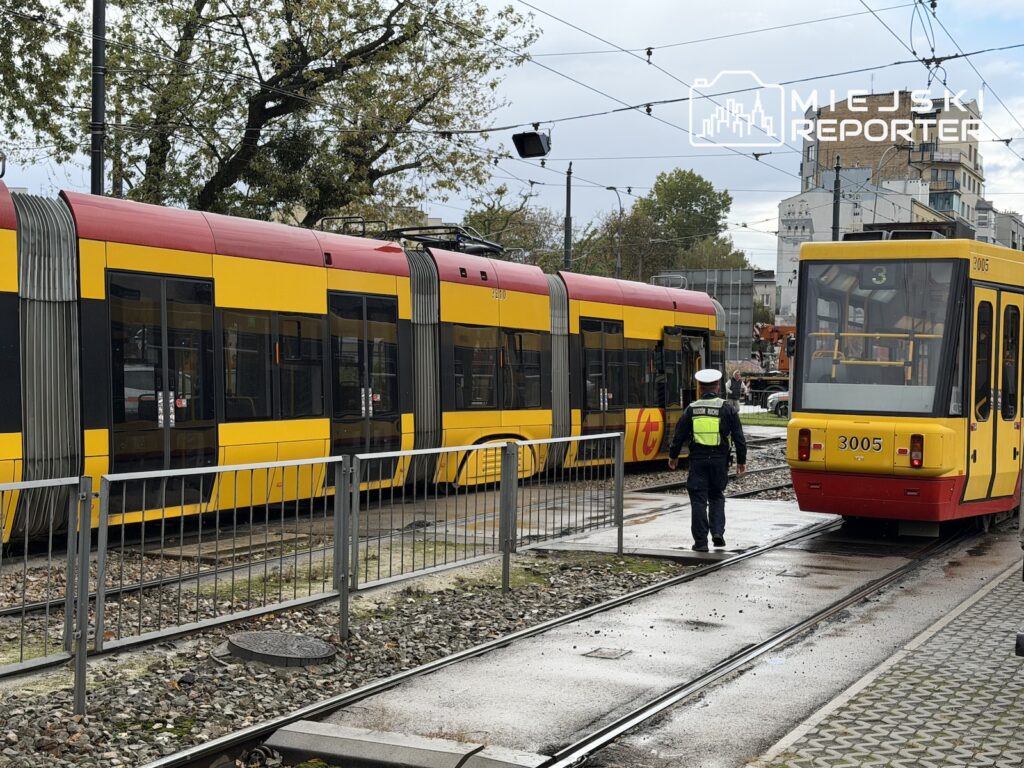 Dwa żółto-czerwone tramwaje stoją na sąsiednich torach, obok nich pracownik w kamizelce odblaskowej.