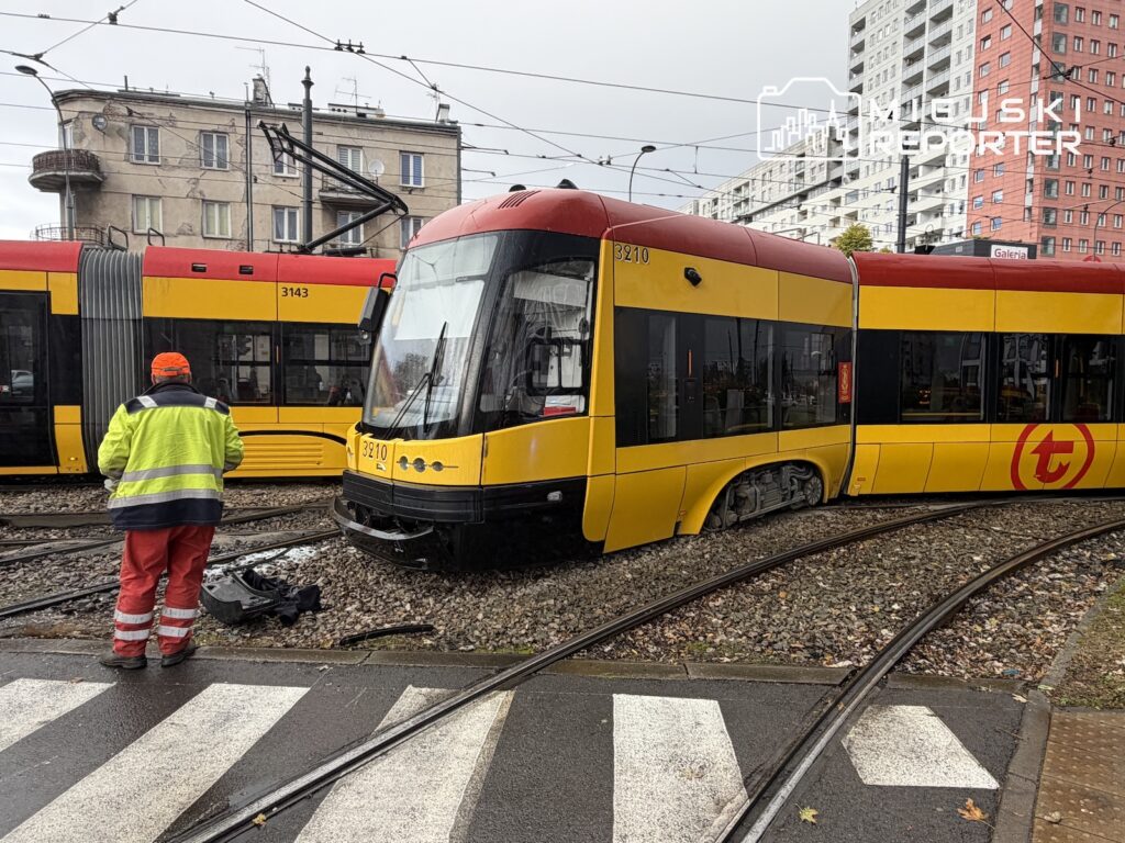 Żółto-czerwony tramwaj stoi poza szynami przy drugim składzie, obok torowiska pracownik w odblaskowej kurtce.