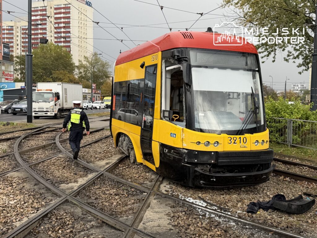 Żółto-czerwony tramwaj stoi na rozjeździe torów, obok torowiska idzie pracownik w kamizelce odblaskowej.