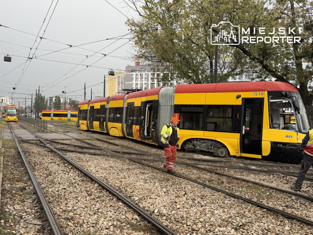 Żółto-czerwony tramwaj stoi na torowisku, a pracownik w odblaskowym stroju przechodzi obok składu.