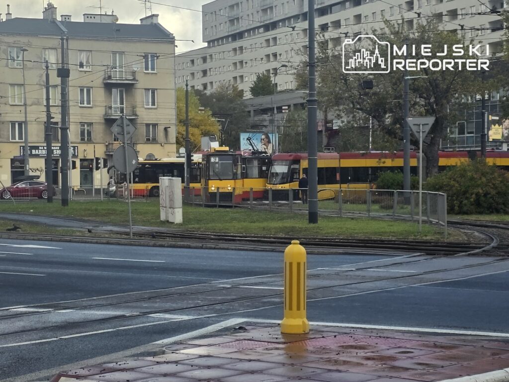 Czerwono-żółte tramwaje stoją na torach obok siebie, na tle miejskich budynków.