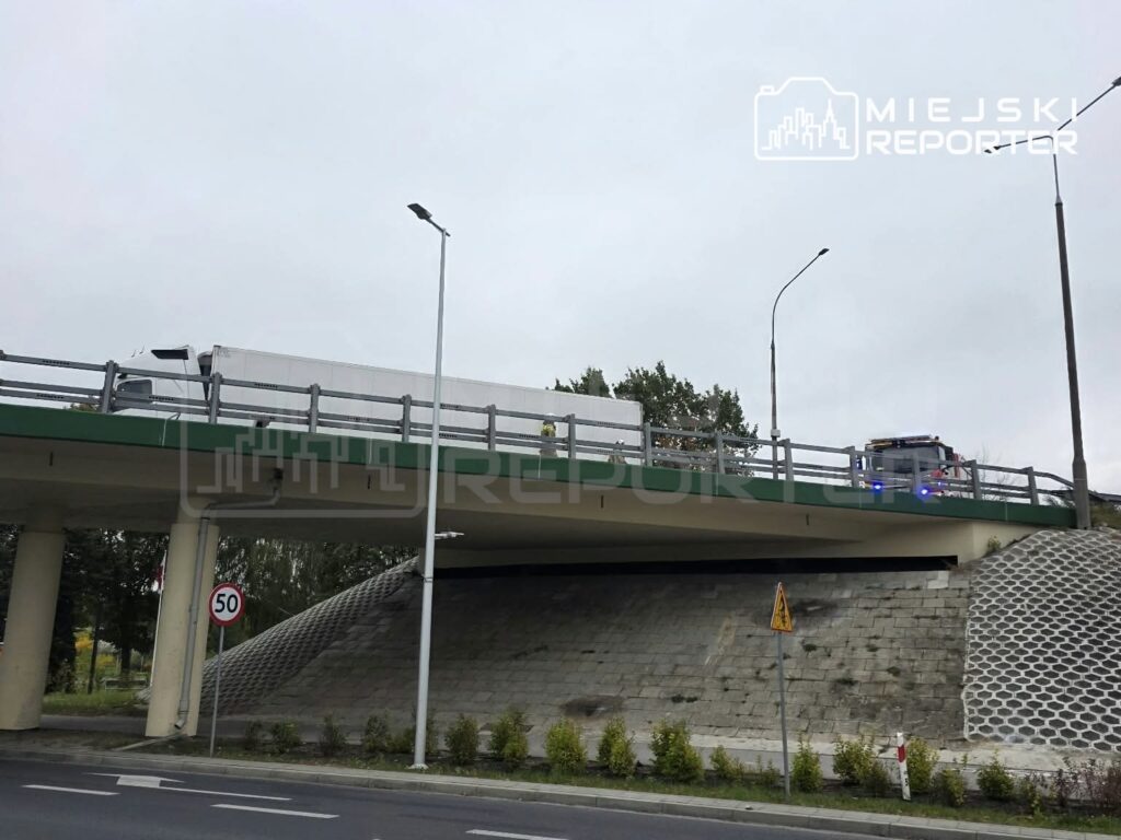 Ciężarówka i pojazd służb na wiadukcie nad ulicą, przy znaku ograniczenia prędkości do 50 km/h.