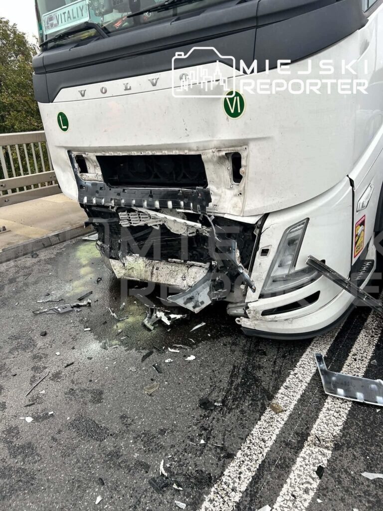 Biała ciężarówka Volvo z rozbitym przodem stoi na jezdni, a wokół niej leżą fragmenty karoserii.