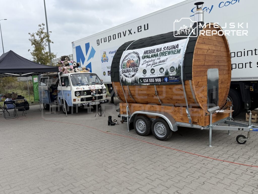 Drewniana mobilna sauna na przyczepie stoi obok ozdobionego pluszakami vana, pod namiotem i przy ciężarówce.