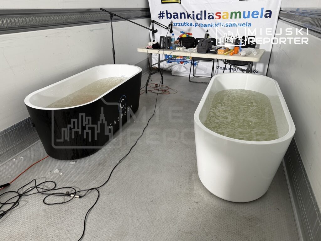 Dwie wanny z wodą stoją w pomieszczeniu; na stole za nimi widnieje baner „#bankidlasamuela”.