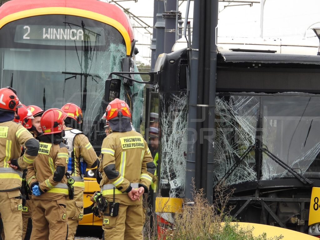 Strażacy oglądają uszkodzone pojazdy; szyby tramwaju są rozbite, a przednia szyba autobusu popękana.