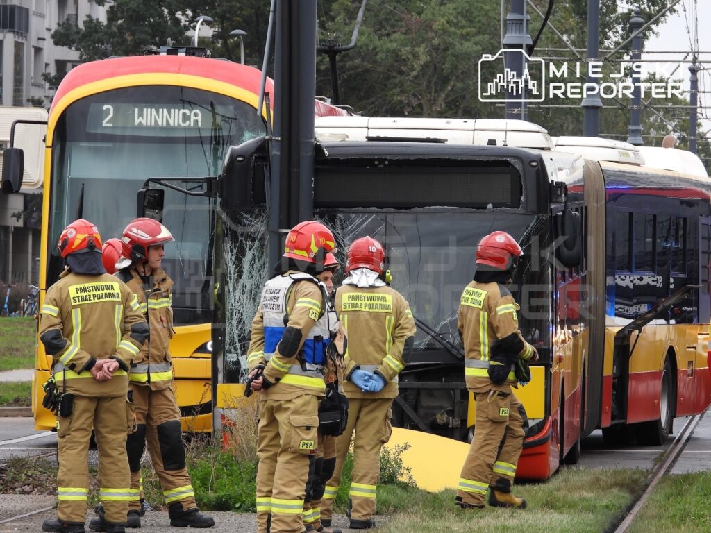 Strażacy w hełmach stoją przed uszkodzonymi autobusami i tramwajem na torowisku.