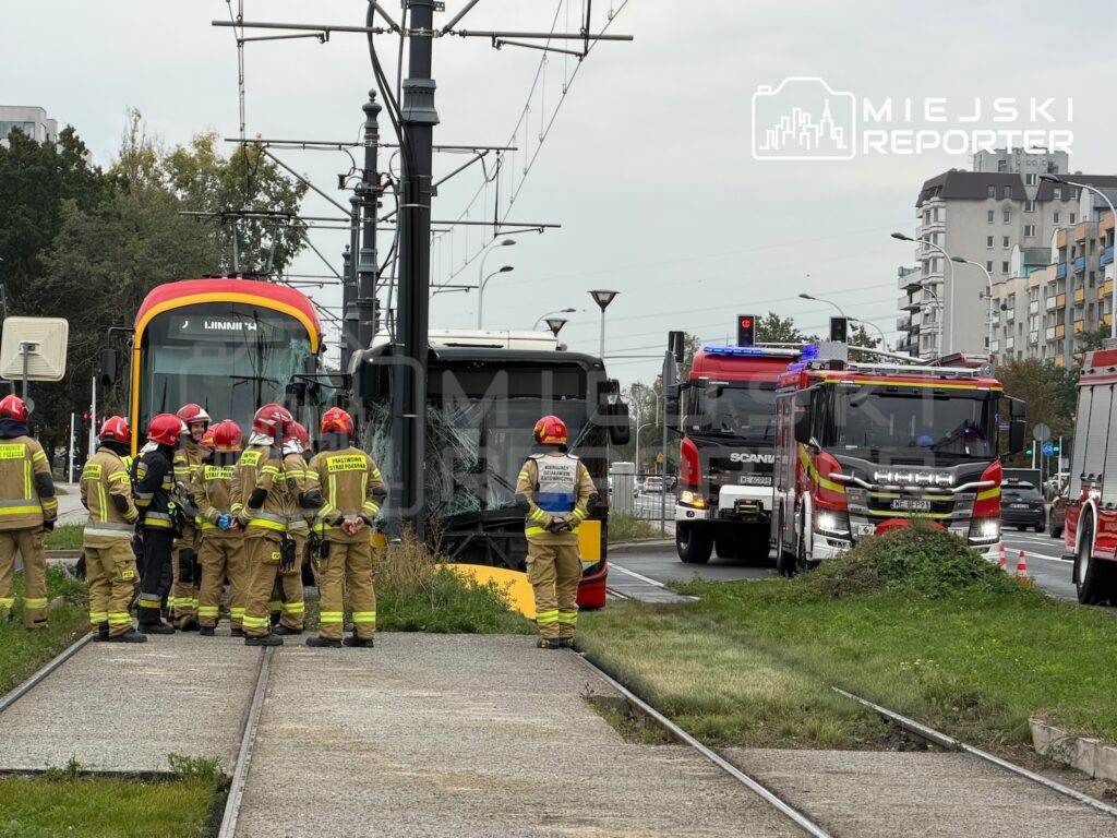 Strażacy stoją przy autobusie i tramwaju na torowisku, obok wozu strażackiego z włączonymi sygnałami.